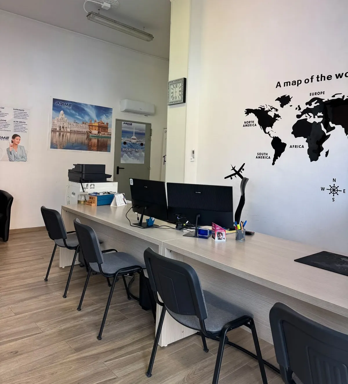 L'interno dell'ufficio Prime Travel: scrivanie con i computer e una mappa del mondo alla parete